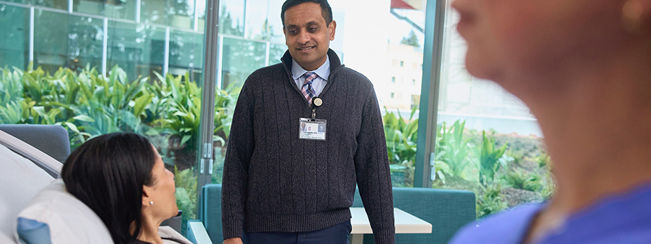 A doctor smiles as he stands next to a patient in bed.