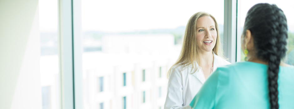 Dr. Antonia Gragg, a certified physician associate and instructor of neurology at the OHSU School of Medicine, stands in front of a large window speaking with a patient.
