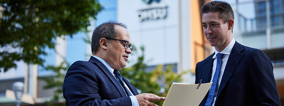 Two doctors stand outside an OHSU building discussing a document.