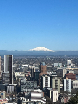 Portland skyline with a snow-capped mountain visible in the distance under a clear blue sky.