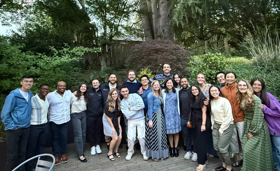 A large group of 22 people pose leaning in together outside in a garden.