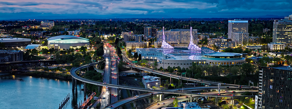A photo shows a sweeping dusk view of Southeast Portland where Interstate 5 runs between the Moda Center and the Oregon Convention Center. 