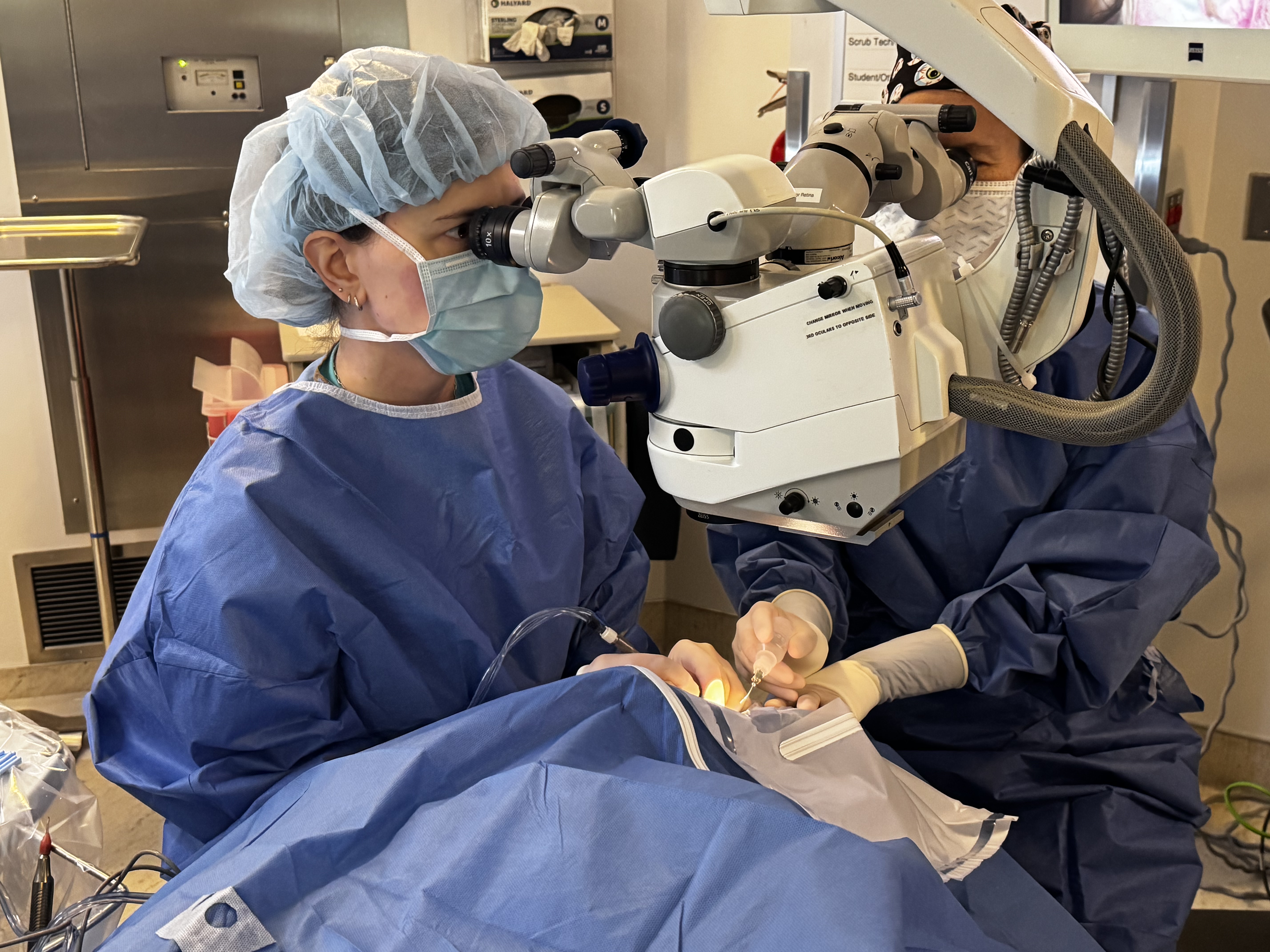 Two surgeons look through microscopes while performing eye surgery.