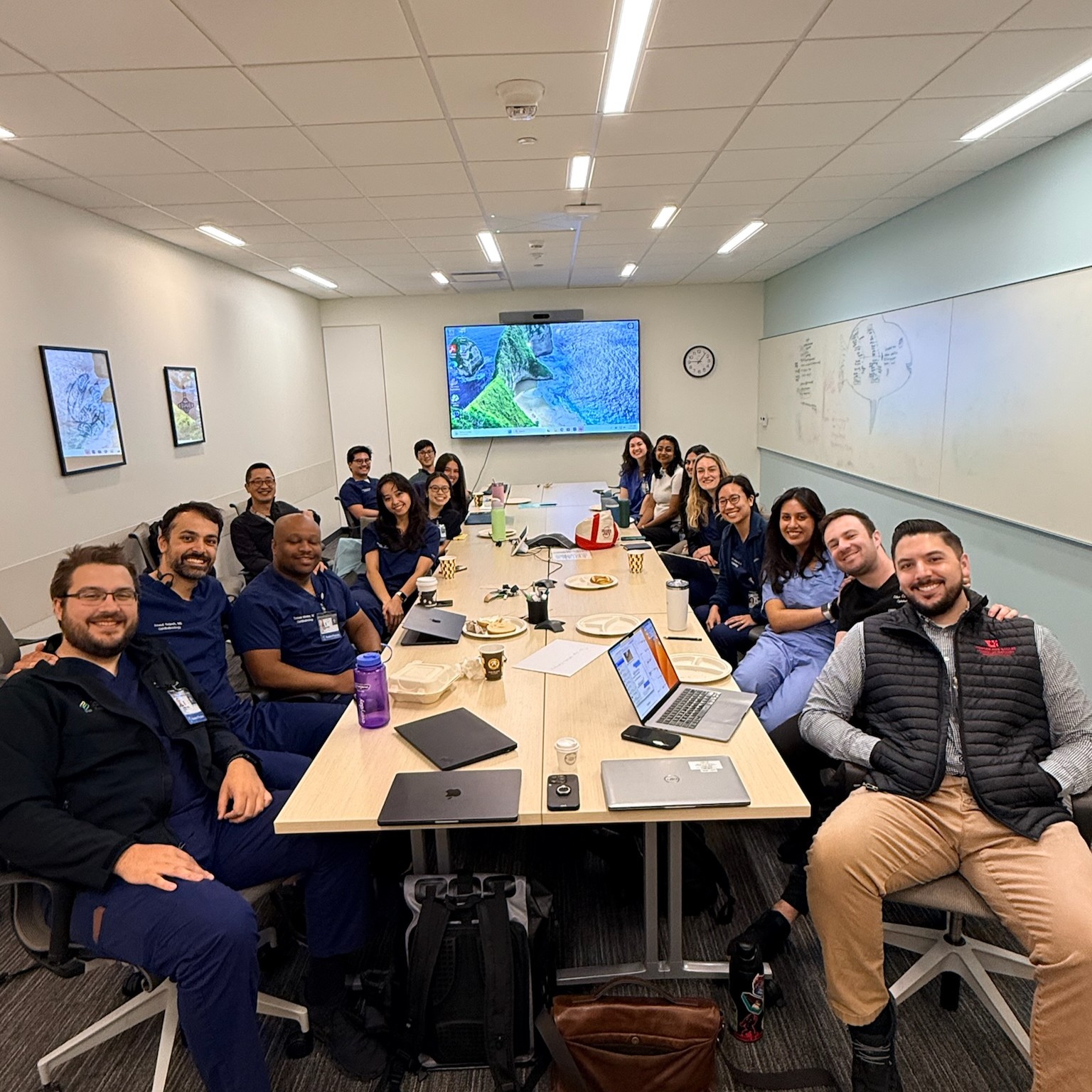 A large group of people sitting at a long conference table lean in to pose for the camera.