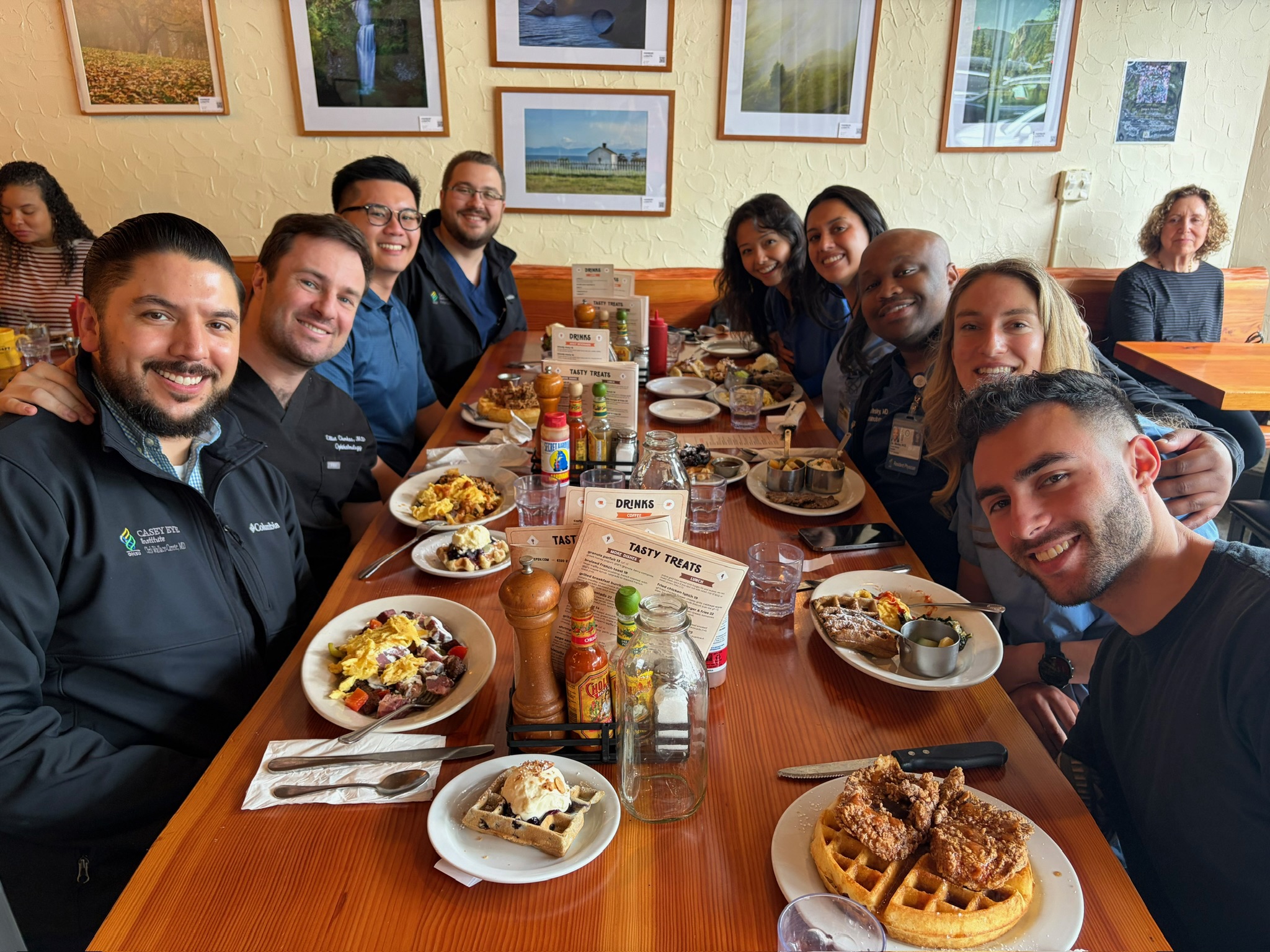 A group of people lean in to pose for the camera with their brunch plates while sitting at a long table in a restaurant.