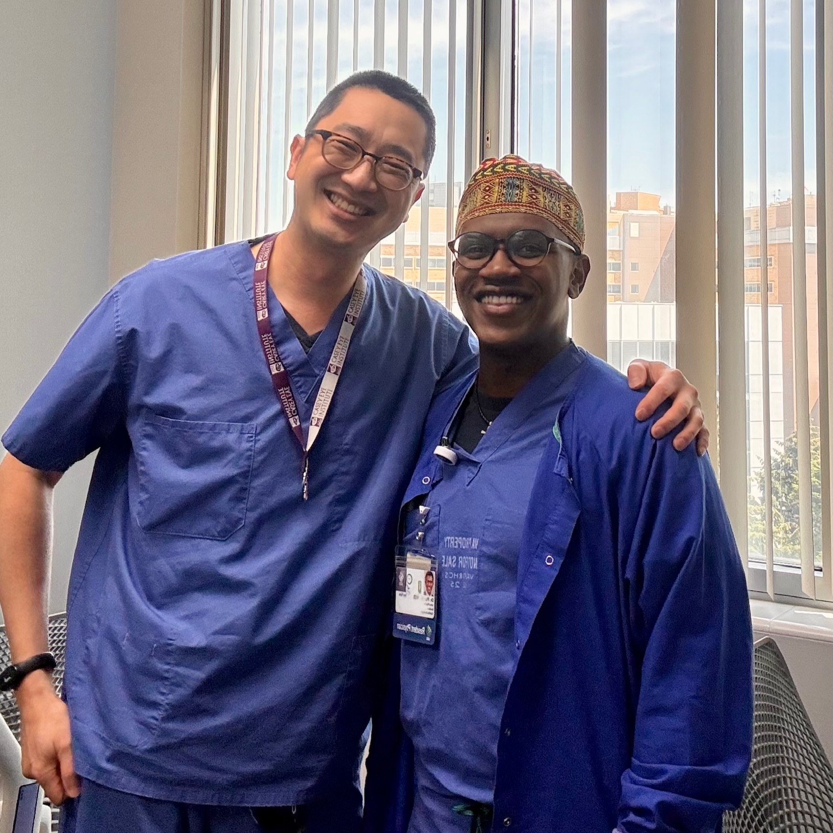 Two men stand side by side in blue scrubs posing for the camera