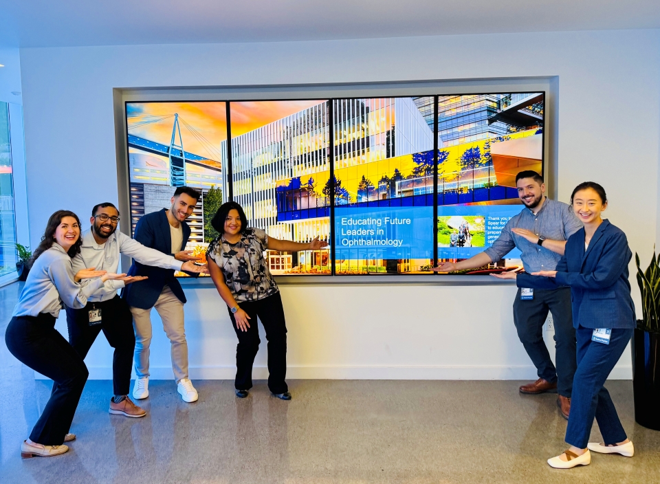 A group of six people pose around a large digital display of the Casey Eye Institute building.