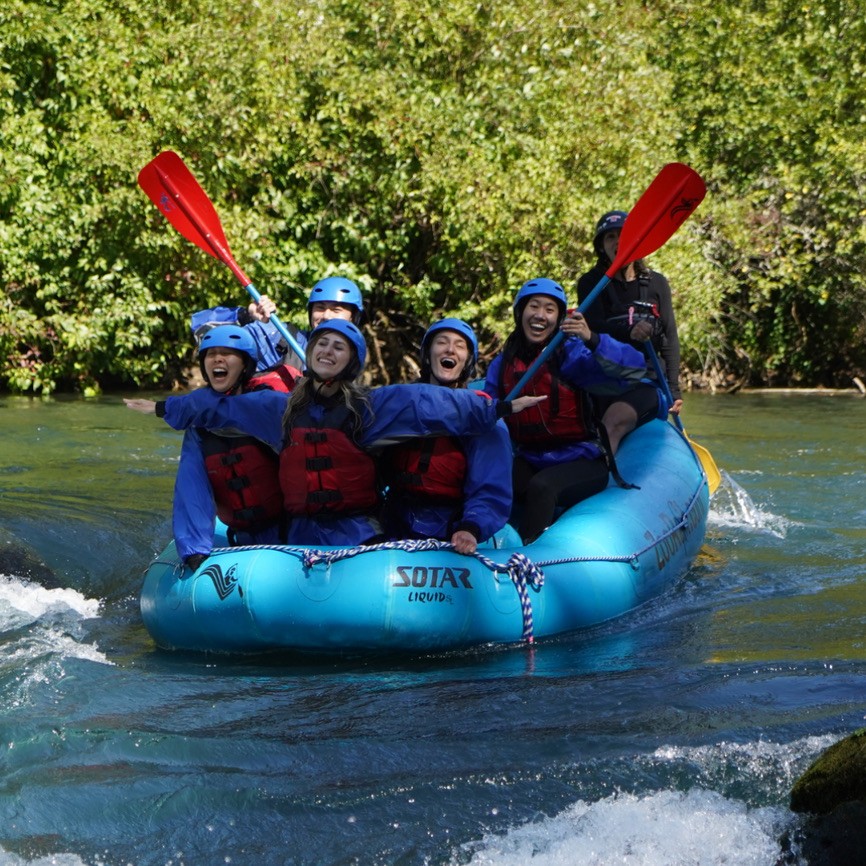 A group of people wearing helmets and life jackets raft down a river.