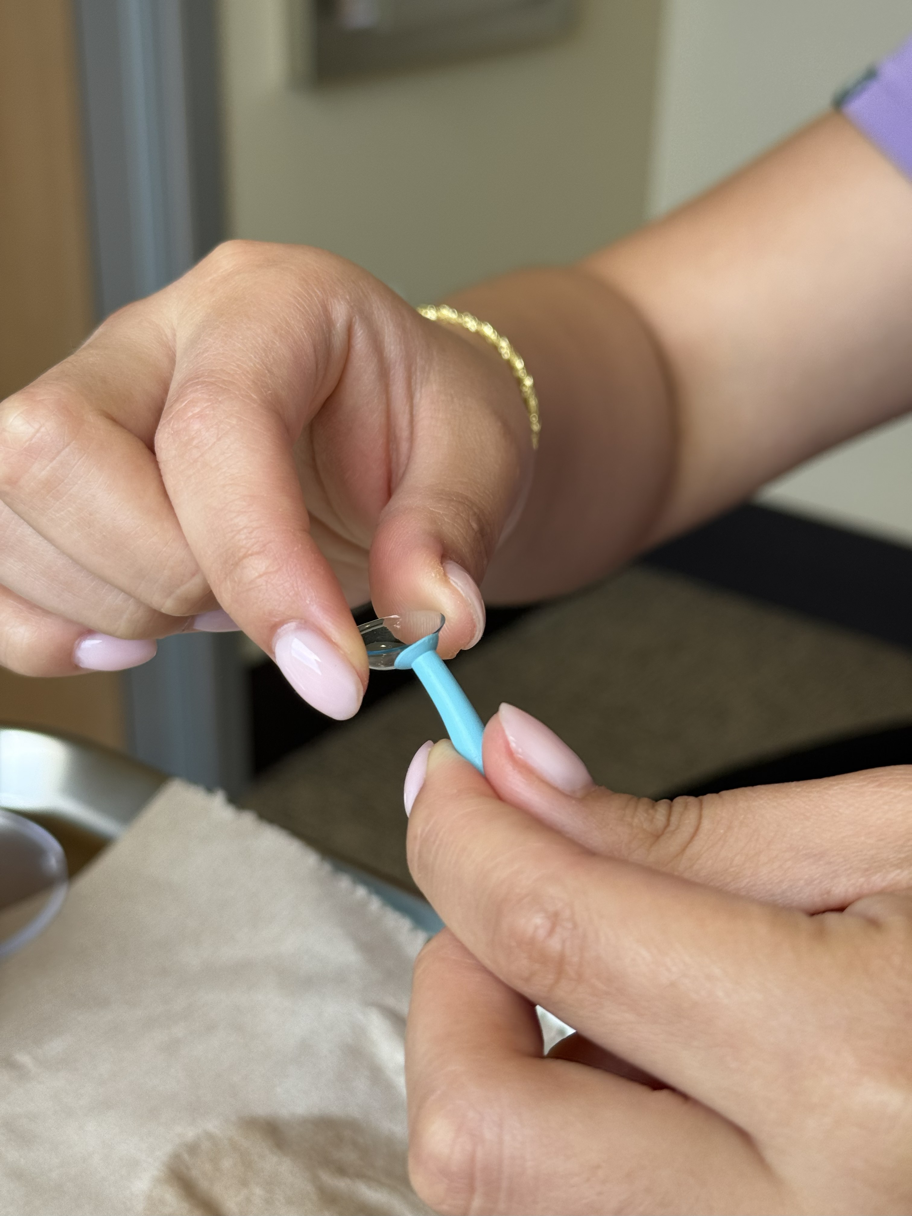 A close up of a person's hands removing the scleral lens from the plunger tool.