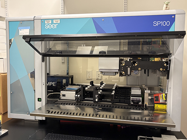 Seer Proteograph SP100 laboratory instrument with its front panel open, showing sample trays and automated pipetting components.