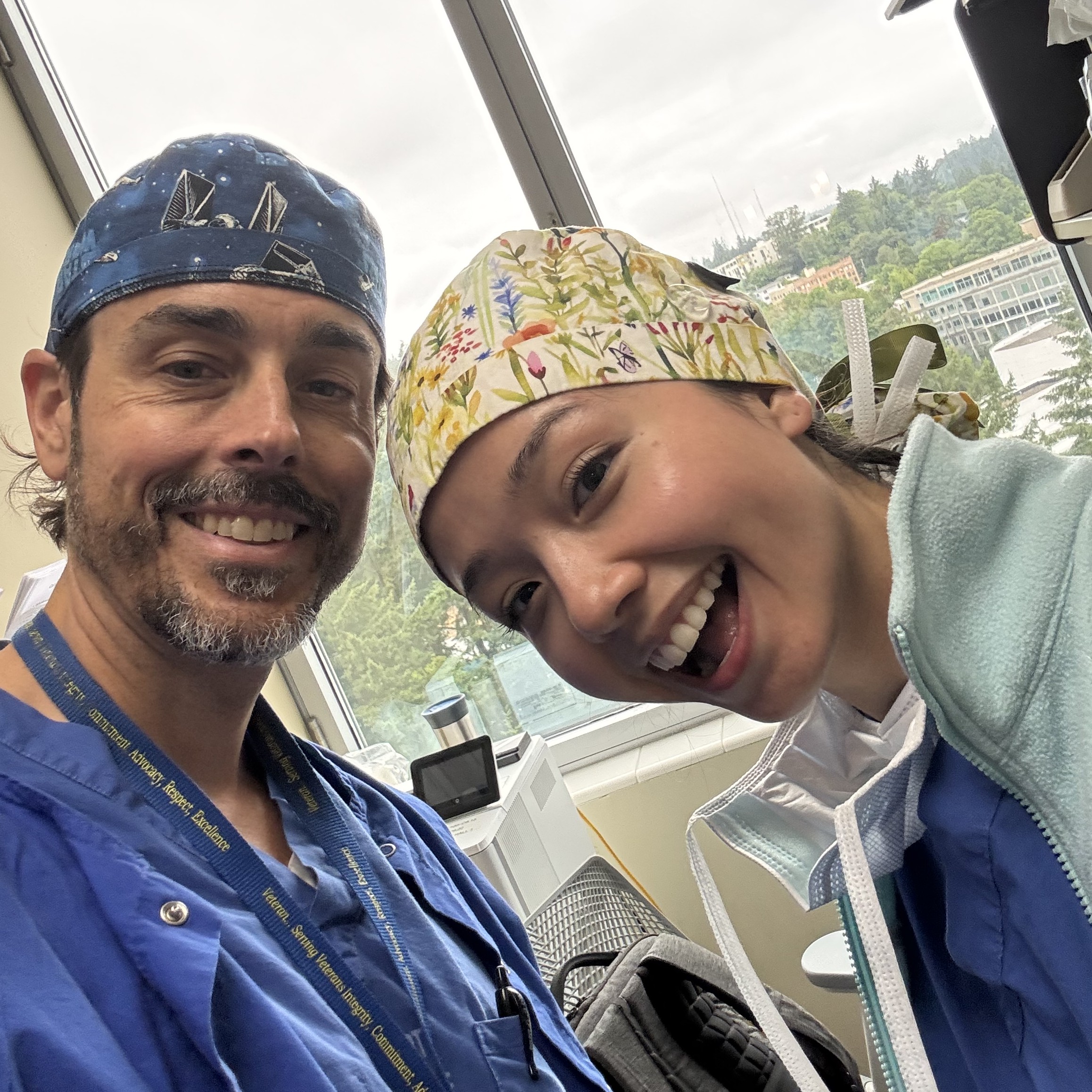 Two people smile while taking a selfie. They are wearing scrubs from the OR.