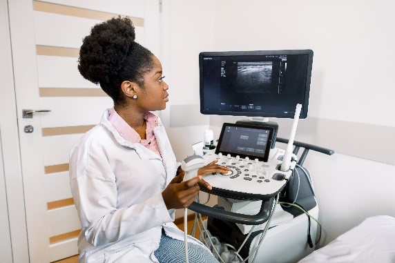 Young African American female doctor in white coat using ultra ultrasound scanning machine and looking on the screen. African woman doctor working on modern ultrasound equipment