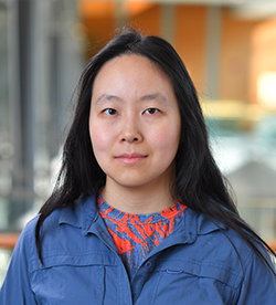 Dr Helen Yang is facing the camera in front of a blurry background.