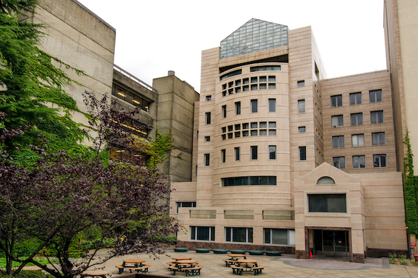 Tall brick building with pointed glass top with a square with picnic tables in front