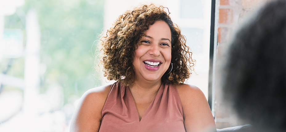 Smiling patient in front of window with out-of-focus back of head of provider in foreground.